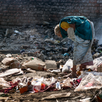 A woman leans over looking at rubbish strewn on the ground